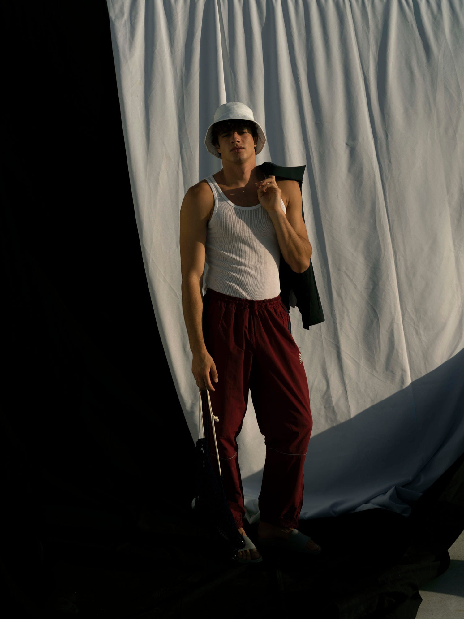 Man with a bucket hat and red pants stands in frond of a white background