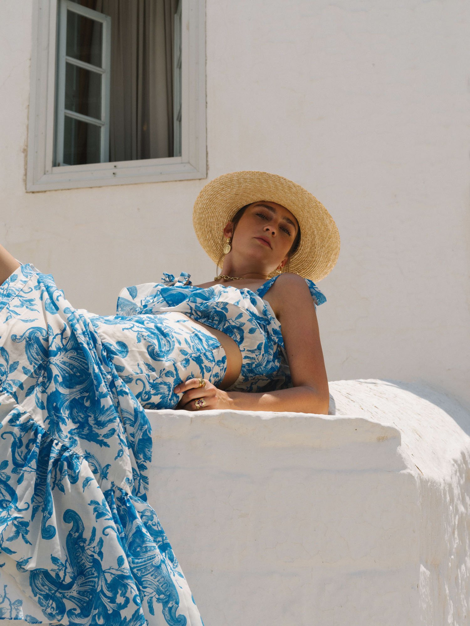 Girl on a summer dress and a straw hat sitting on a fench