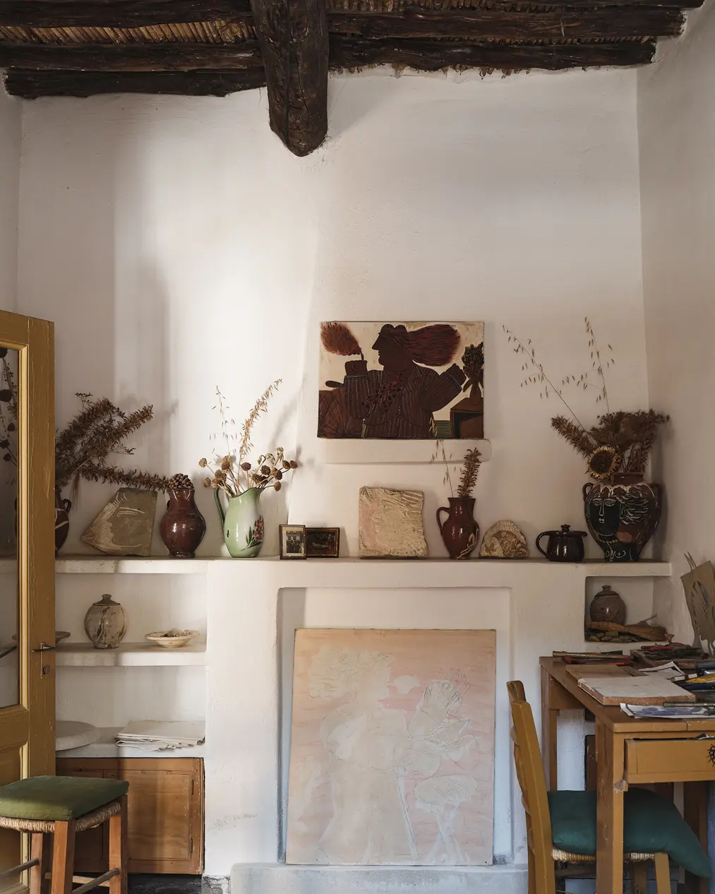 Artist’s desk surrounded by pottery, artworks, and rustic ceiling beams inside Alekos Fassianos’ house.