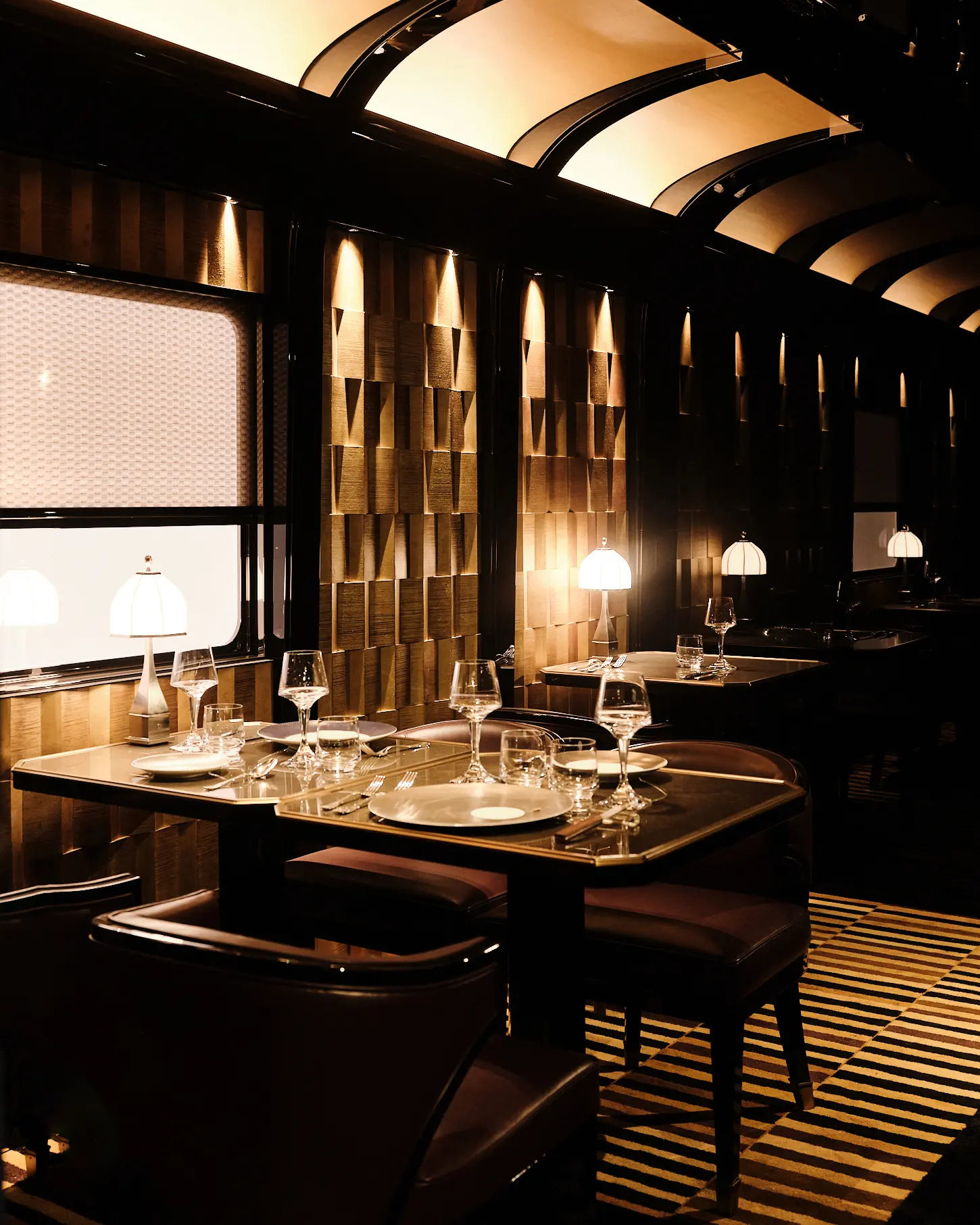 The Dining Car — Light, Brass, and Pattern Modern Orient Express dining car interior with golden geometric wall panels, brass lamps, and elegantly set tables.