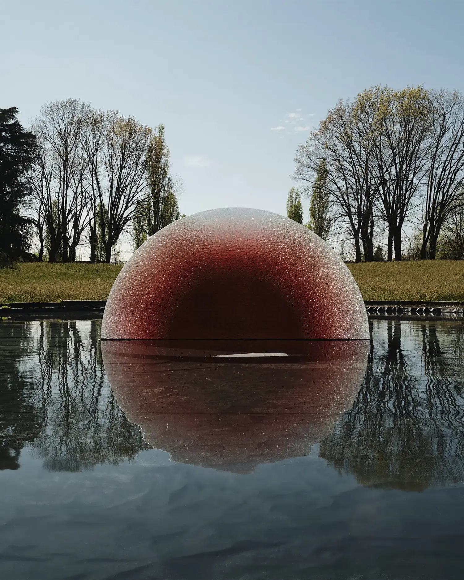 “Sun Catcher” solar art installation by Rive Roshan x SOL R&D at Villa Bagatti Valsecchi, a red dome-like arch reflected in water, evoking the illusion of the sun.