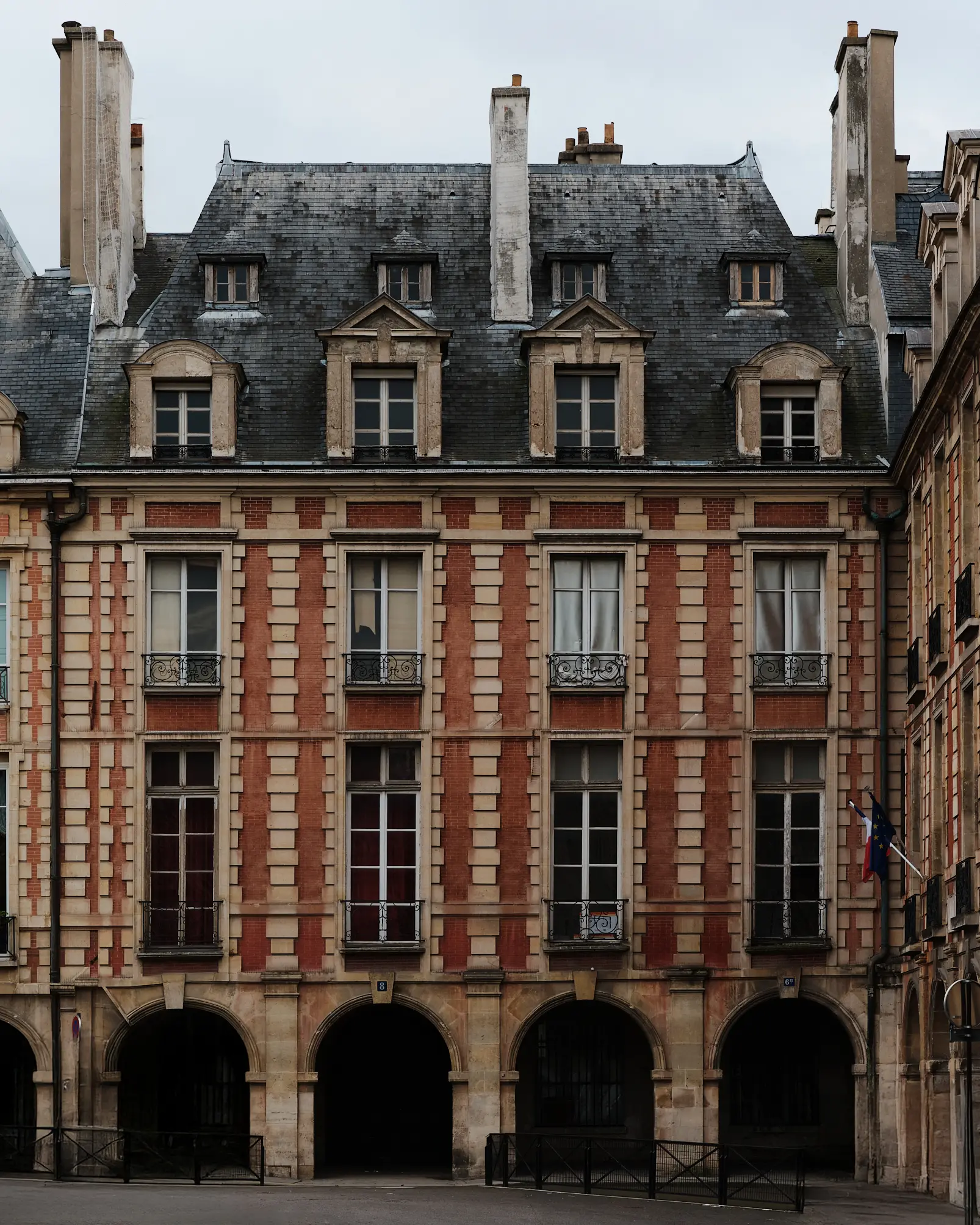 Maison de Victor Hugo — Place des Vosges Façade Historic Parisian façade of Maison de Victor Hugo at Place des Vosges, featuring red brick masonry, stone arcades, wrought-iron balconies, and a slate mansard roof.