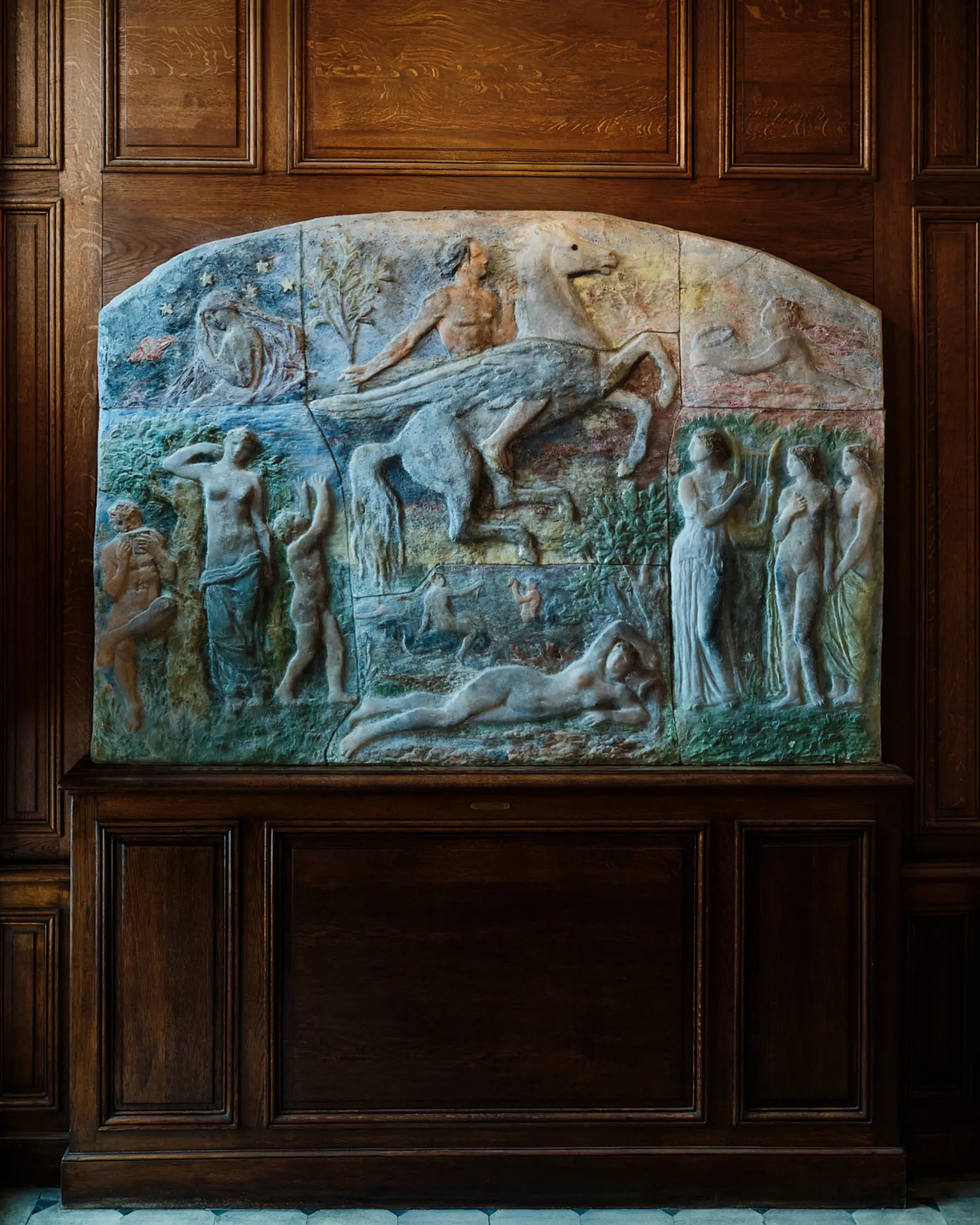 Stone relief sculpture depicting mythological figures mounted on dark wooden paneling inside Maison de Victor Hugo, Paris.