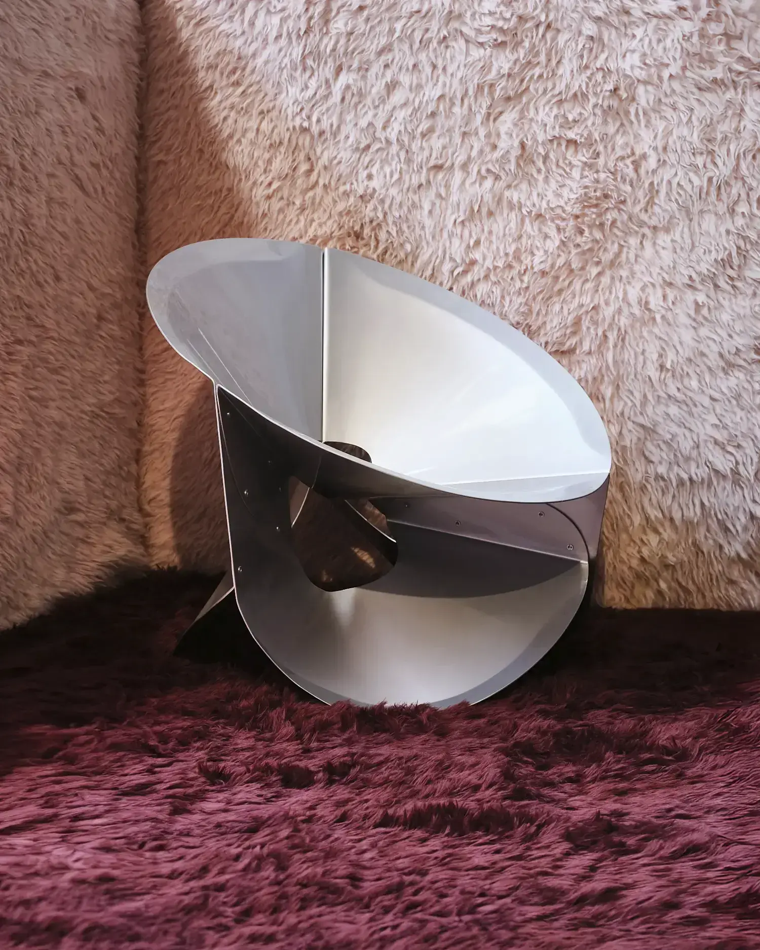 Curved metal side table with intersecting planes set against fur-covered walls at Nilufar Gallery.
